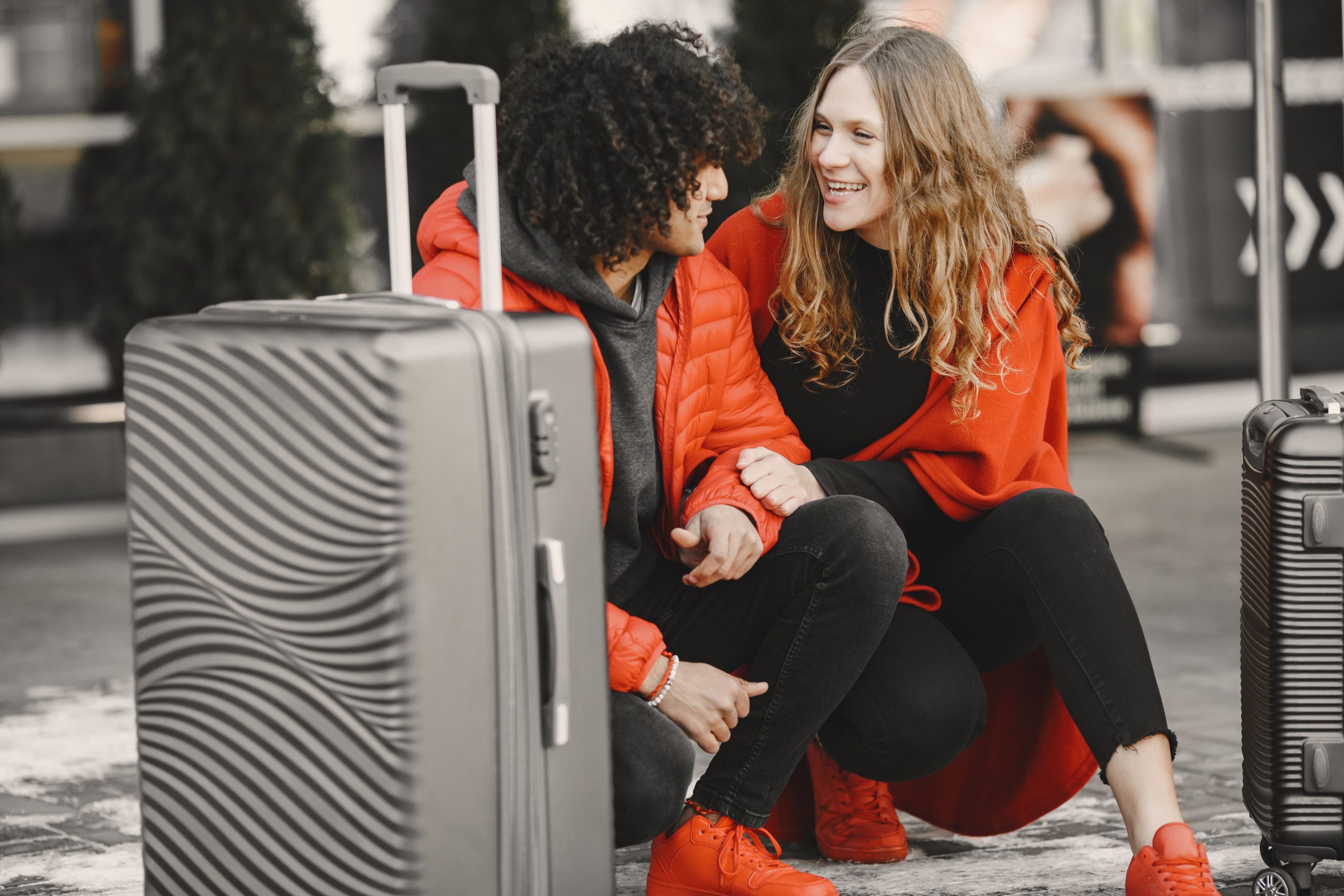 Smiling couple sitting with luggage, enjoying travel together in bold red outfits.